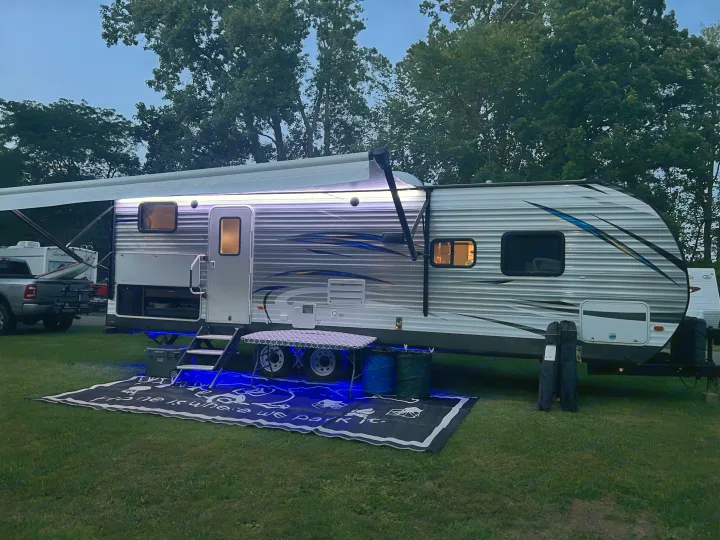 This RV rental glows with blue ground lights and white awning lights at a peaceful evening campsite, featuring a welcome mat.. Forest River Salem 2019