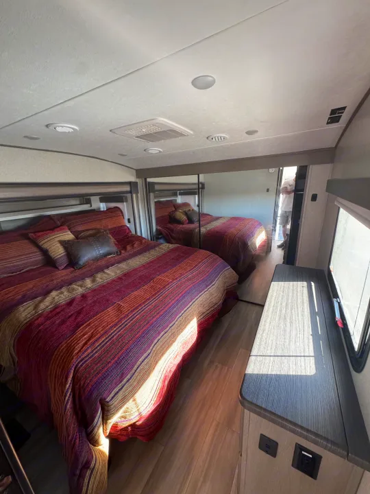 Spacious RV rental bedroom boasts a striped bed, mirrored closet, and counter with ample light. Relax on your next trip.. Coachmen Chapparal 336 TSIK 2022