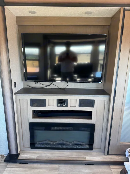 Inside this RV rental: a modern entertainment unit featuring a TV, integrated sound system, and electric fireplace.. Coachmen Chapparal 336 TSIK 2022