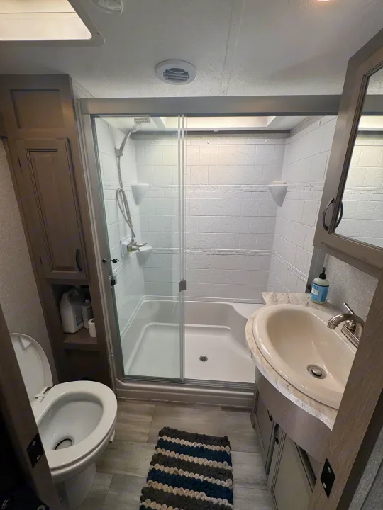 RV rental bathroom: view of toilet on left, glass shower enclosure in center, and sink vanity on right with storage.. Coachmen Chapparal 336 TSIK 2022