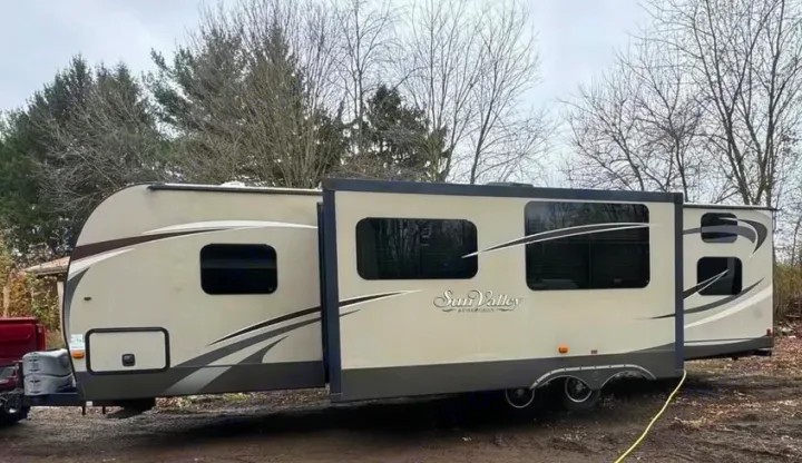 Spacious beige travel trailer RV, ideal for an RV rental, with extended slide-outs parked outdoors in a natural setting.. Evergreen RV Sun Valley 2014