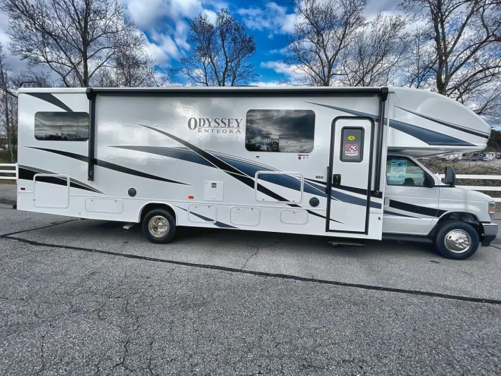 Side view of a large white Class C RV for rent, featuring black and gray graphics. Ideal for your next road trip adventure.. Entegra Odyssey 2025
