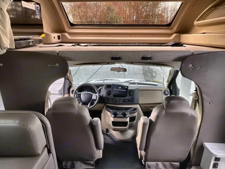 Spacious RV rental interior looking toward the cockpit, overhead bunk, and front window revealing a treed landscape.. Entegra Odyssey 2025
