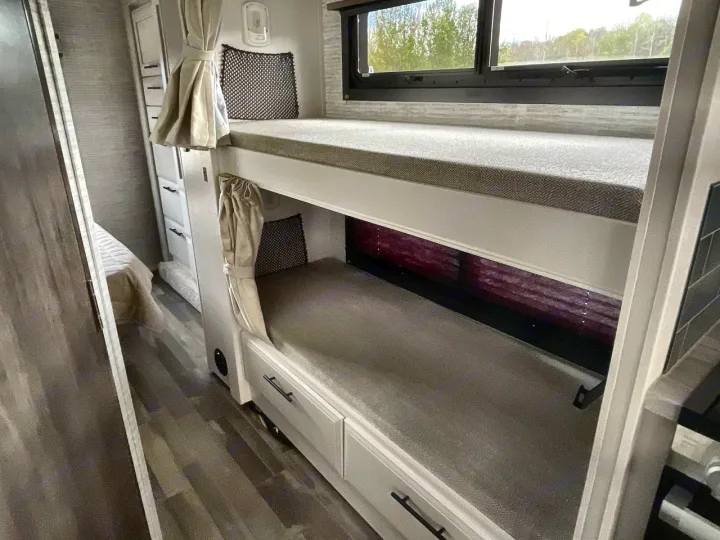 RV rental interior featuring comfortable stacked bunk beds with privacy curtains, storage drawers below, and a large window above the top bunk.. Entegra Odyssey 2025
