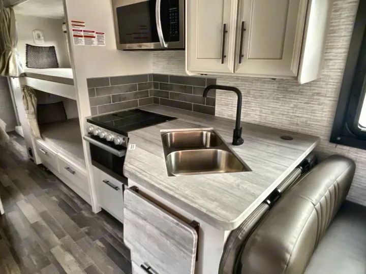 RV rental interior: modern kitchen, sink, stove, microwave, and comfy bunk beds.. Entegra Odyssey 2025