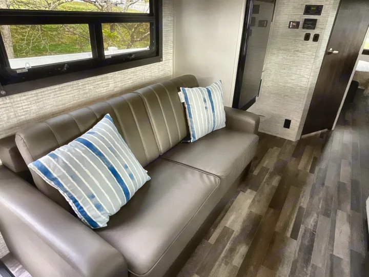 Comfortable RV rental living space with a soft sofa, striped pillows, and a scenic window view. Ideal for your travel adventure.. Entegra Odyssey 2025
