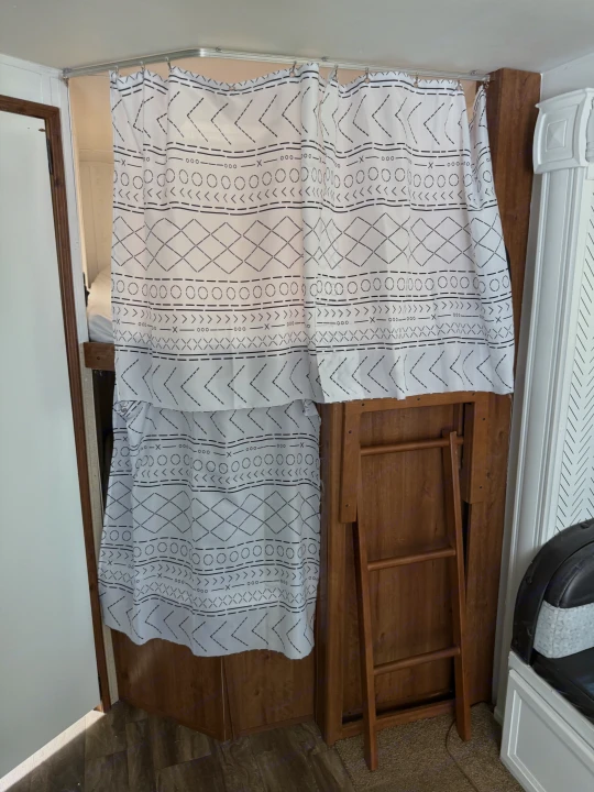 RV rental bunk area with a white and black patterned privacy curtain on a curved track, and a wooden ladder for access.. Gulf Stream Conquest 2016