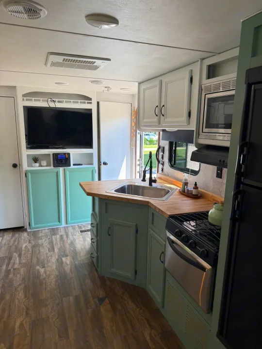 Refurbished rv rental interior featuring a modern kitchen with mint green cabinets, wood counters, and a cozy TV living space.. Gulf Stream Conquest 2016