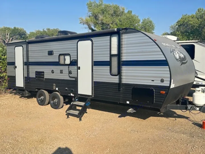 RV rental: Grey and black travel trailer with blue stripe, dual axles, and steps, parked on gravel for camping.. Forest River Cherokee Grey Wolf 2020