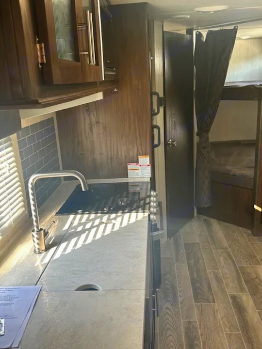 RV rental kitchen featuring a sink, covered stovetop, and ample cabinet space. A private bunk area with curtain is to the right.. Forest River Cherokee Grey Wolf 2020
