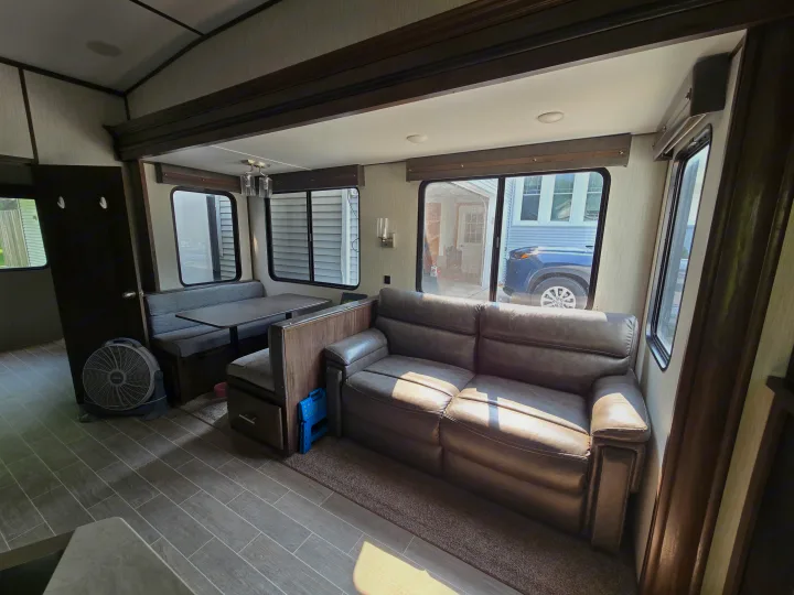 Inside an RV rental: Bright living area with a grey dinette, brown sofa, tiled floor, and multiple windows.. Forest River Cherokee Arctic Wolf 2019