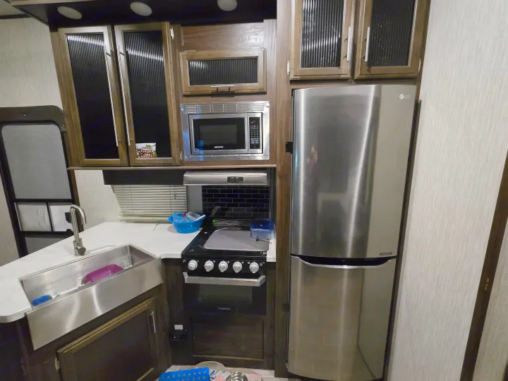 RV rental kitchen: stainless steel LG fridge, Greystone microwave, Furrion oven, sink, and dark wood cabinets.. Forest River Cherokee Arctic Wolf 2019