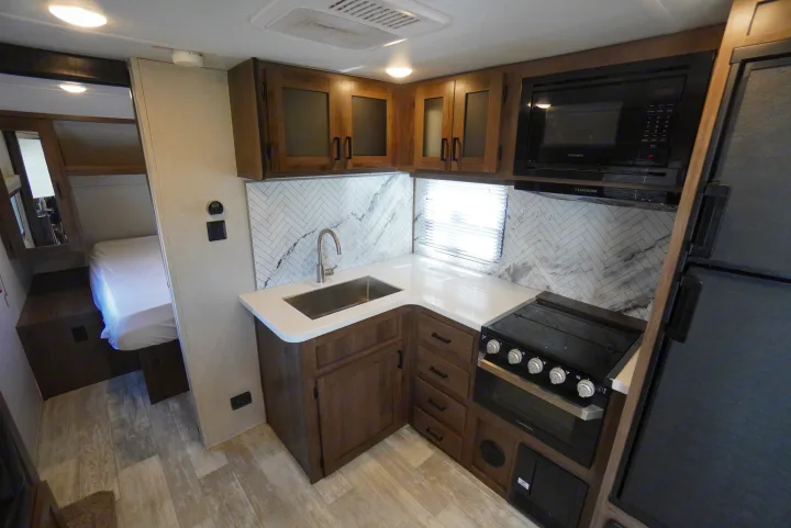 RV rental with a sleek kitchen: white counters, stainless sink, oven, microwave, and bright bedroom beyond.. Forest River Tracer 2021