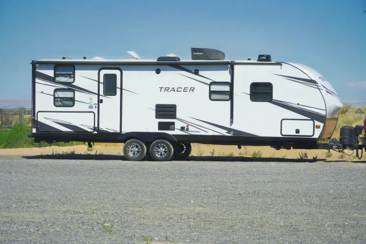 This white travel trailer RV, ideal for an rv rental, is parked on gravel under a clear blue sky.. Forest River Tracer 2021