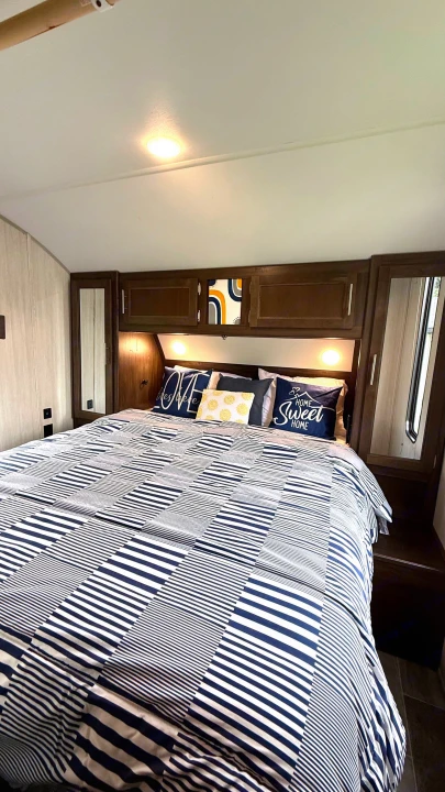 Comfortable RV rental bedroom featuring navy & white striped bedding, built-in wooden cabinetry, & soft lighting.. Forest River Cherokee Grey Wolf 2019