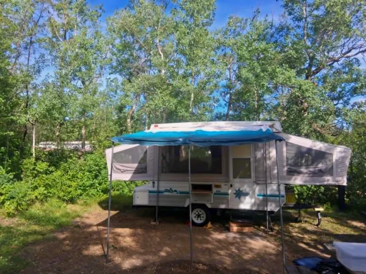 Pop-up camper RV rental nestled in a sunny, green forest campsite, ready for outdoor adventure.. Bonair 1050C 1996