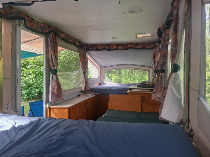 Spacious pop-up camper interior, ideal for an RV rental getaway. Features two beds, cabinets, and panoramic nature views.. Bonair 1050C 1996