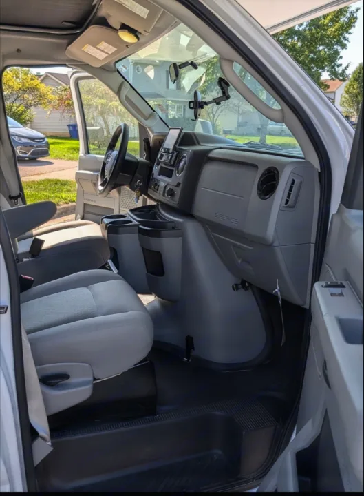 Interior view of an RV rental van's front cabin, showcasing the clean dashboard, steering wheel, and comfortable gray seats.. Forest River Coachmen Freelander 2021