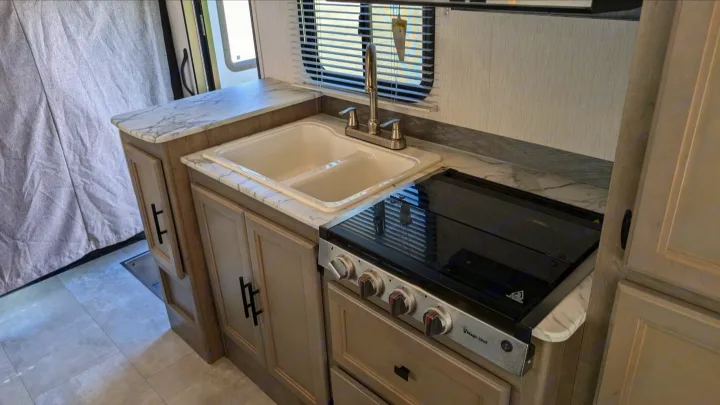 Modern RV rental kitchen with dual sink, stove, marble-look counters, and light wood cabinets, ready for use.. Forest River Coachmen Freelander 2021