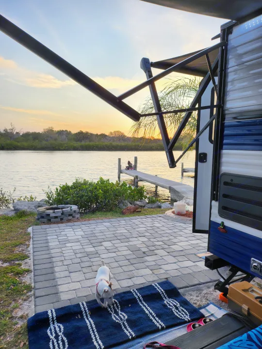 Waterfront RV rental offers a paved patio, dock with a person, and a white dog under a sunset sky.. Sunset Park RV Sun Lite 2022