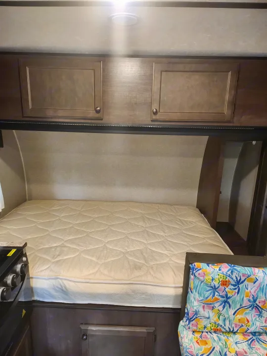 RV rental bedroom features: a comfy quilted mattress, wood cabinets, LED lighting, and a colorful tropical pillow.. Sunset Park RV Sun Lite 2022