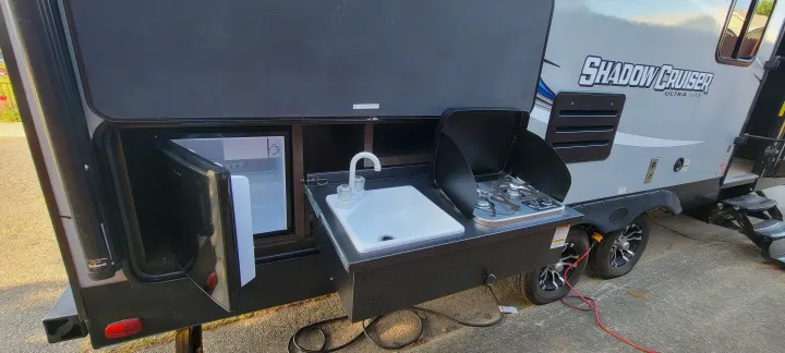 Outdoor kitchen setup on an RV rental, featuring a mini-fridge, sink, and two-burner stove for camping.. Shadow Cruiser 240RBH 2019