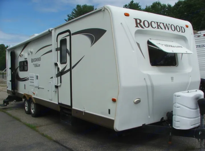 This white Rockwood travel trailer, perfect for an rv rental, is seen from the side, showcasing its front window and entry door.. Rockwood Signature Ultra Lite 2012
