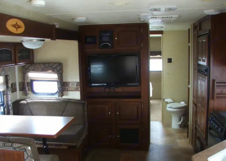 RV rental interior: Dinette, TV entertainment center, kitchen area with appliances, and a visible toilet in the bathroom.. Rockwood Signature Ultra Lite 2012