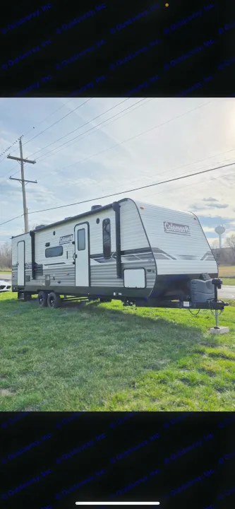 Explore new destinations with this Coleman travel trailer RV rental. The sleek white and grey camper is parked outdoors on green grass.. Dutchmen Coleman Lantern 2022