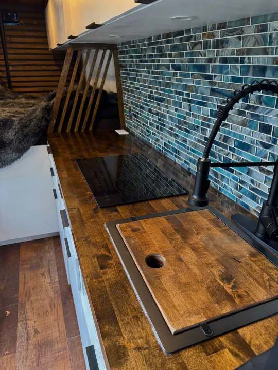 Modern RV rental kitchen with wood counters, induction cooktop, and blue tile backsplash.. Mercedes-Benz Sprinter 2020