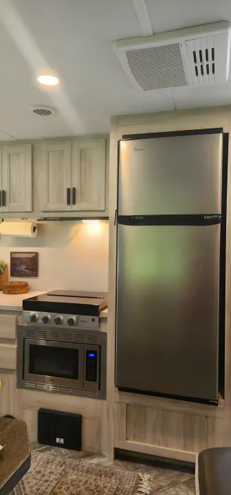 Modern RV rental kitchen with stainless steel appliances (fridge, microwave, cooktop), light wood cabinets, and bright lighting.. Forest River Sunseeker LE 2022