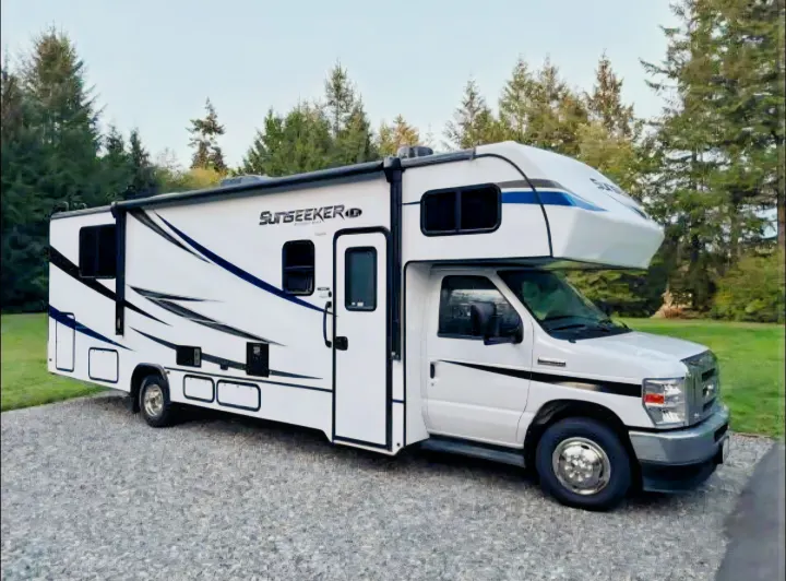 This clean white **rv rental** motorhome is parked on gravel, ready for adventure amidst green trees.. Forest River Sunseeker LE 2022