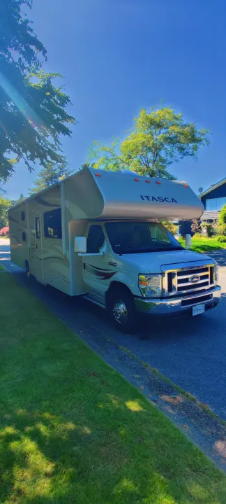 Sunny Class C Itasca RV rental parked on a street with green trees and grass, ready for adventure.. Itasca Spirit 2014