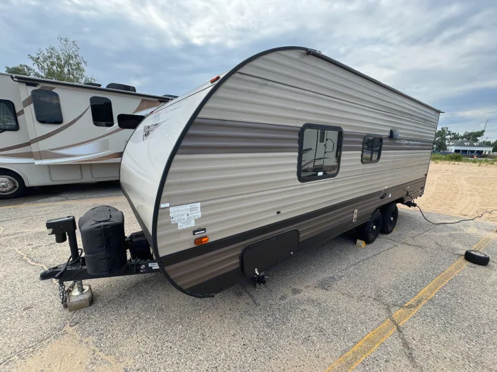 RV rental: A two-axle travel trailer camper, grey and brown, parked on asphalt with a motorhome behind it.. Forest River Wildwood X-Lite 2019