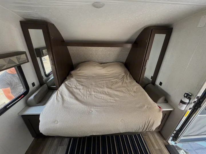Inside this RV rental: A cozy bedroom with bed, overhead shelf, and storage cabinets, offering comfort on the road.. Forest River Wildwood X-Lite 2019