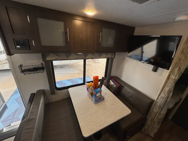 Enjoy this RV rental's comfortable interior: a dinette with snacks, overhead storage, a TV, and an outdoor view.. Forest River Wildwood X-Lite 2019