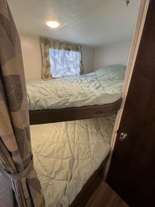 RV rental interior features two bunk beds with comfy light comforters, a window, and a door. Ideal sleeping area.. Forest River Wildwood X-Lite 2019