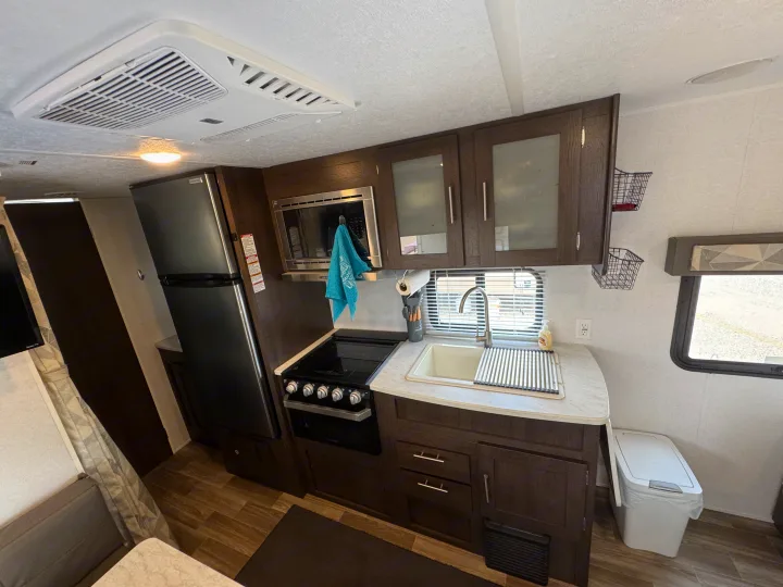Modern RV rental kitchen featuring a fridge, stove, microwave, and sink, highlighting a functional and well-equipped interior.. Forest River Wildwood X-Lite 2019