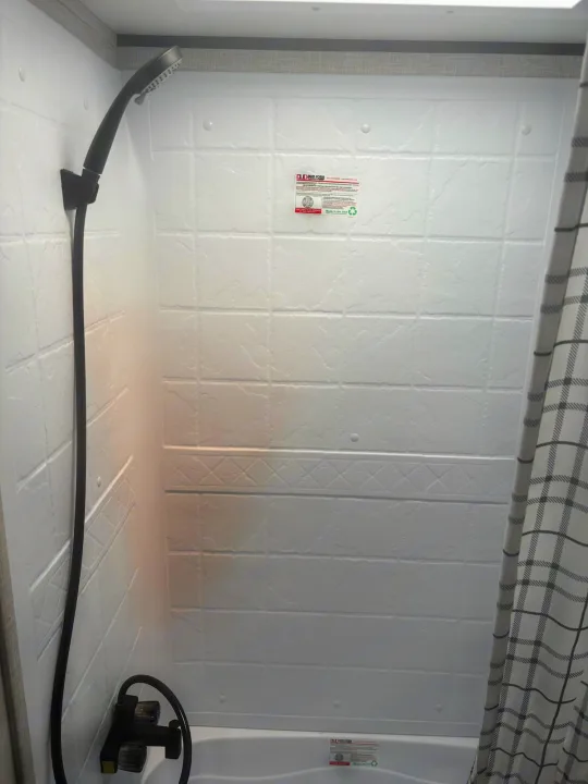 Step inside this RV rental's shower, featuring a compact design, black shower head, and plaid curtain.. Jayco Jay Flight SLX 2025