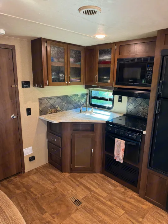 RV rental kitchen: features a well-equipped area with a sink, stove, microwave, dark cabinets, and a tiled backsplash.. Forest River Palomino Puma 2018