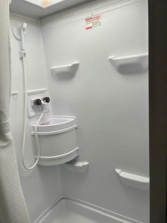 Compact RV rental shower featuring a small sink, handheld shower, and shelves, all in white.. Forest River R-Pod 2021