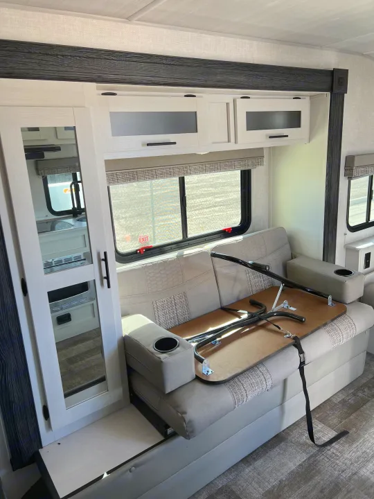 RV rental interior: dinette with patterned seating & cupholders, stowed table, overhead cabinets, and mirrored closet.. Forest River R-Pod 2021