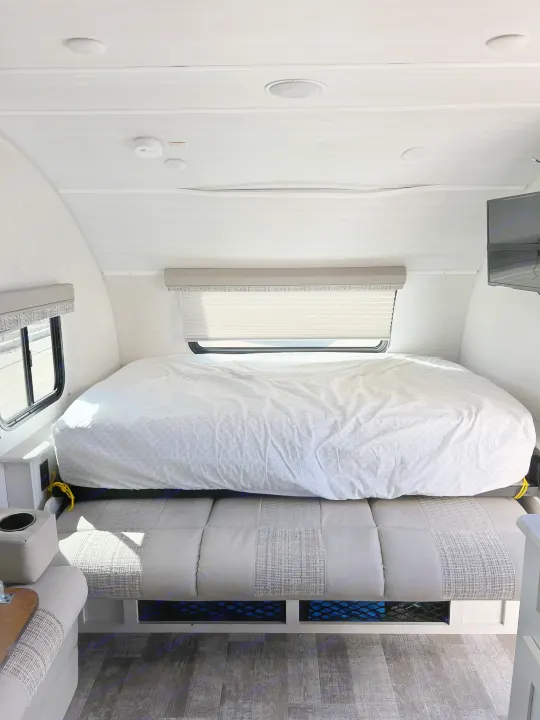 Cozy RV rental bedroom featuring a large bed with a light patterned duvet, side windows, and a convertible sofa/dinette.. Forest River R-Pod 2021