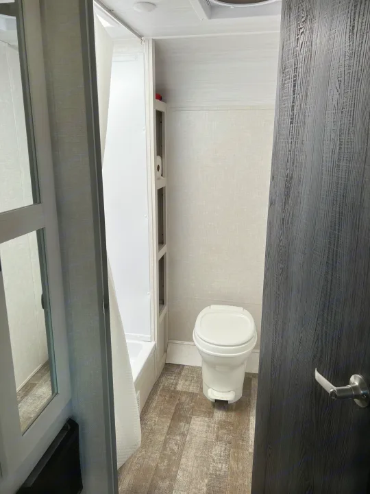 Clean, functional RV rental bathroom with toilet, shower, storage shelves, and textured wood-look flooring.. Forest River R-Pod 2021