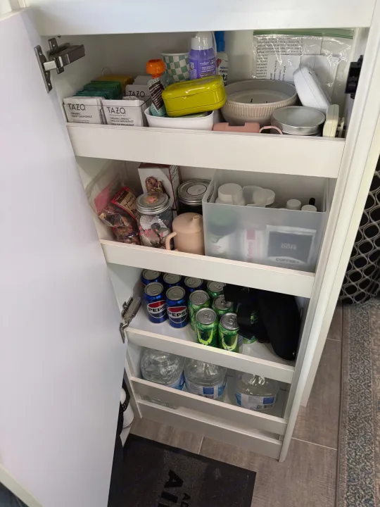 Inside an RV rental, a compact pantry unit neatly holds TAZO tea, snacks, Pepsi, water, and various travel essentials on shelves.. Airstream Caravel 2020