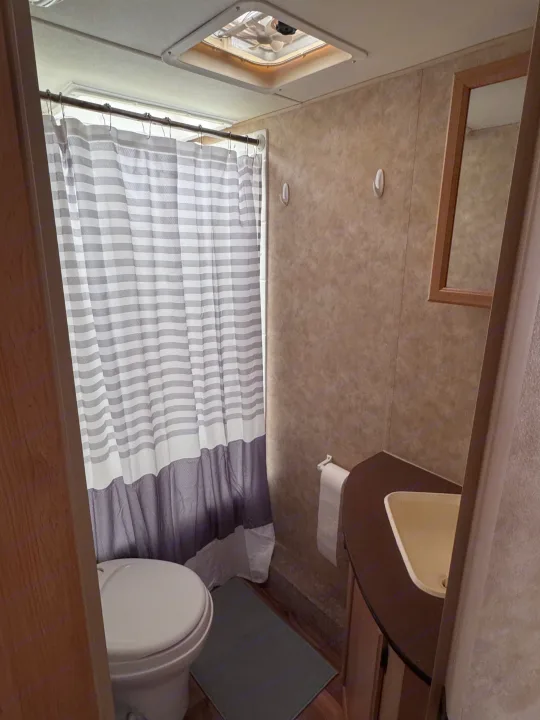 Compact RV rental bathroom features a toilet, striped shower curtain, sink, mirror, and ceiling vent for essential comfort.. kz Coyote 2010