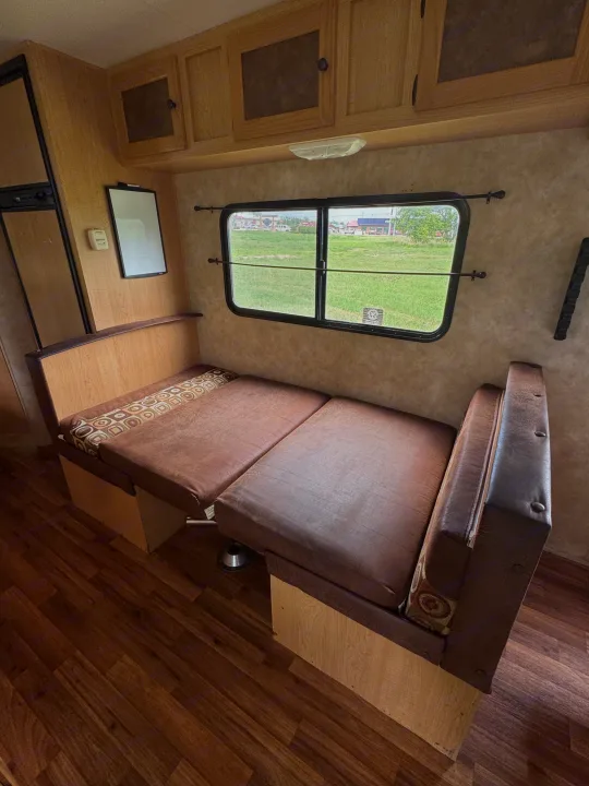 Cozy rv rental interior with brown dinette, overhead cabinets, and a window view of greenery. Perfect for road trips.. kz Coyote 2010