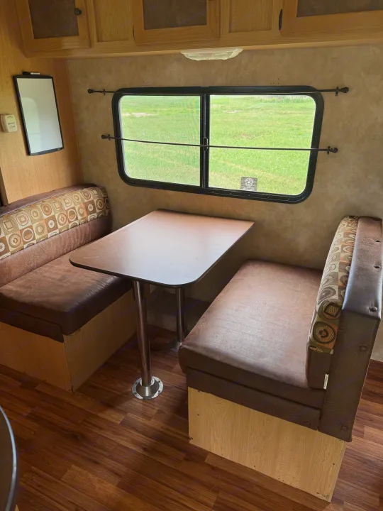 RV rental dinette area featuring brown faux leather benches, a table, and a window overlooking green scenery.. kz Coyote 2010