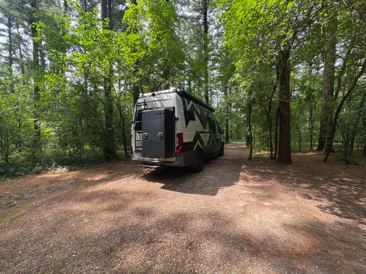 White camper van RV rental parked on a gravel path in a sunny forest, ready for adventure.. Mercedes-Benz Sprinter RV Motorhome Campervan 2022