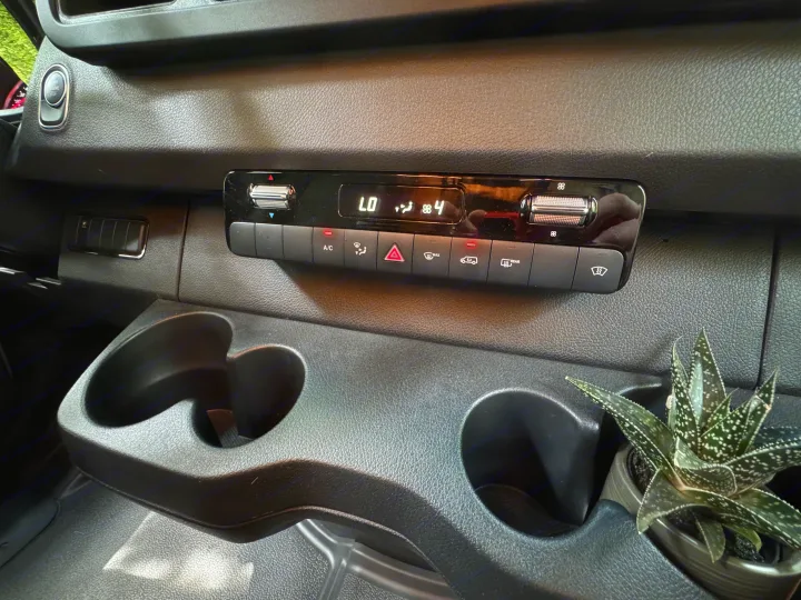 Inside an RV rental: dashboard features climate control, dual cup holders (one with a succulent), and engine start/stop button.. Mercedes-Benz Sprinter RV Motorhome Campervan 2022